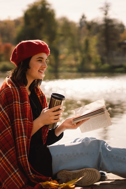 Ein Teengirl in einem roten Barett-Lesebuch auf Holzponton-Herbstsaison