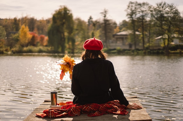 Ein Teengirl in einem roten Barett-Lesebuch auf Holzponton-Herbstsaison