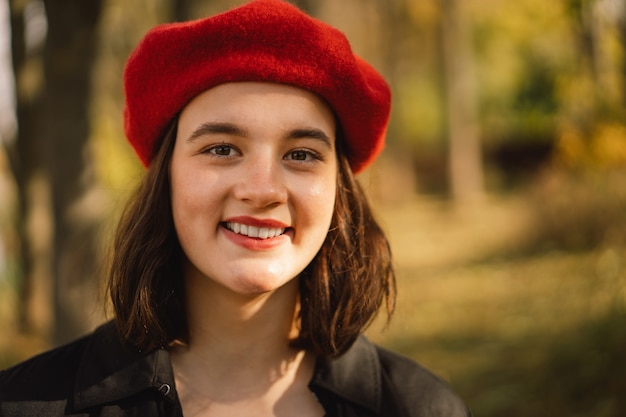 Ein Teengirl in einer roten Baskenmütze mit einem Strauß Herbstblätter in den Händen geht durch den Wald