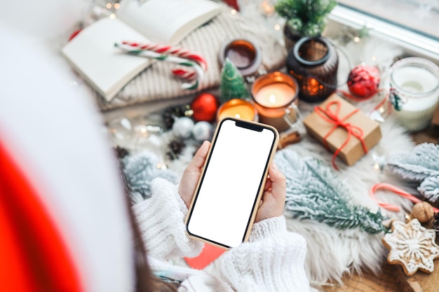 Ein Telefon mit einem isolierten Bildschirm in den Händen eines Kindes vor dem Hintergrund eines festlichen Neujahrsinterieurs ein Platz für Ihren Text