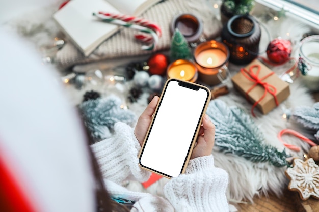 Ein Telefon mit einem isolierten Bildschirm in den Händen eines Kindes vor dem Hintergrund eines festlichen Neujahrsinterieurs ein Platz für Ihren Text