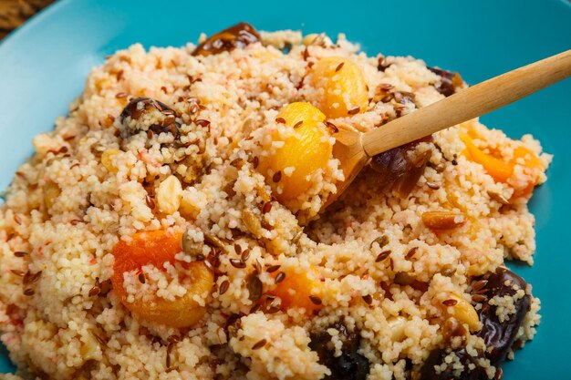 Foto ein teller couscous auf einem holztisch neben dattelnüssen und einem krug obstbrühe ein löffel mit müsli in der hand über einem teller