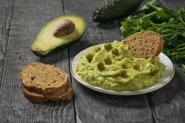 Ein Teller Guacamole mit grünen Erbsen, Brot und Avocadofrucht auf einem Holztisch. Diät-vegetarisches mexikanisches Essen Avocado. Rohkost.