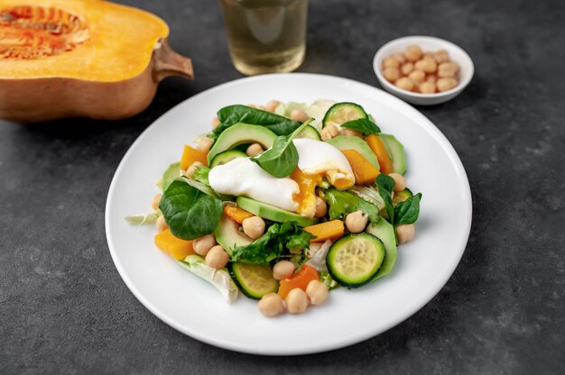 ein Teller mit Avocadosalat, Kichererbsen, Kürbis, Gurke, pochiertem Ei in einem Teller