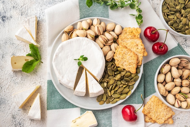 Ein Teller mit Brie, Pistazien, Kürbiskernen, Kirsche.