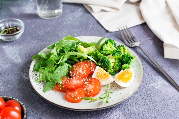 Ein Teller mit Brokkoli-Rucola-Tomate und gekochtem Ei auf einem Teller auf dem Tisch Ketogene Diät