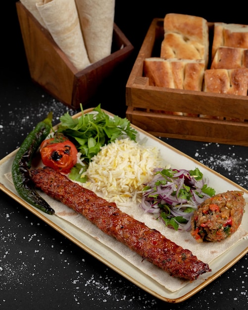 Foto ein teller mit essen mit einem fleischkebab und einer schüssel brot im hintergrund.