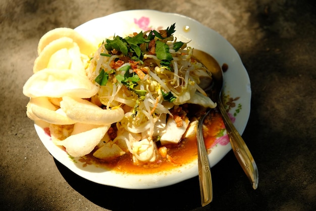 Ein Teller mit Essen mit einem Löffel darauf und einem Löffel auf der Seite Kupat Tahu Indonesisches Essen