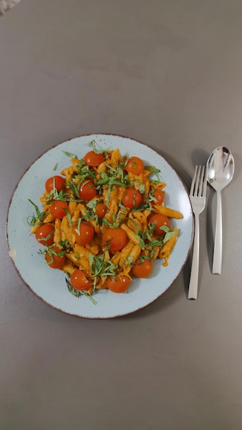 Ein Teller Nudeln mit Tomaten und Parmesan darauf neben einer Gabel und einem Messer.