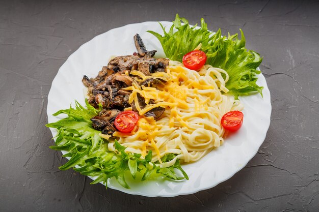 Ein Teller Pasta mit Pilzen und Käse garniert mit Kräutern auf grauem Betonhintergrund. Horizontales Foto