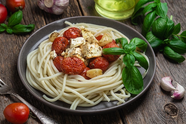 Ein Teller Spaghetti mit Tomaten, Käse und Basilikum auf einem Holztisch.