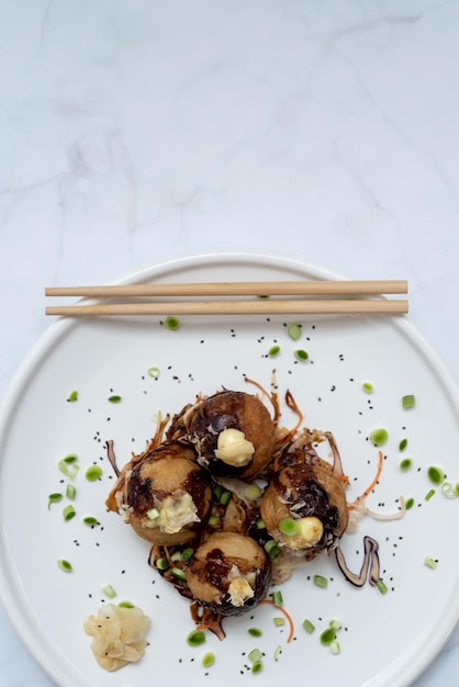 Ein Teller Takoyaki mit Essstäbchen über einem Marmortisch