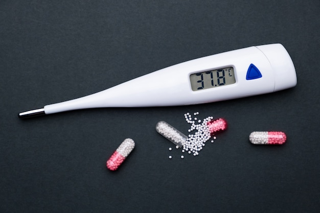 Ein Thermometer und Medizin auf einem schwarzen Hintergrund. Behandlung eines Coronavirus, einer Grippe oder einer Erkältung. Medizinisches Konzept