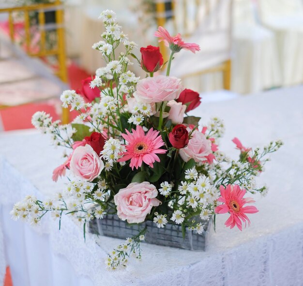 Ein Tisch mit einer Blumenvase darauf und einer weißen Tischdecke mit roten und rosa Blumen darauf.