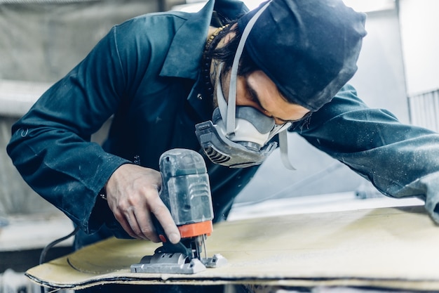 Ein Tischler schneidet ein Brett mit einer elektrischen Stichsäge. Herstellung von Skateboards.