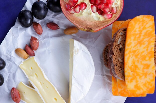 Ein tolles Produkt für ein Frühstück Käse mit Früchten, Nüssen und einem Glas Milch auf Pergamentpapier auf blauem Hintergrund, Nahaufnahme