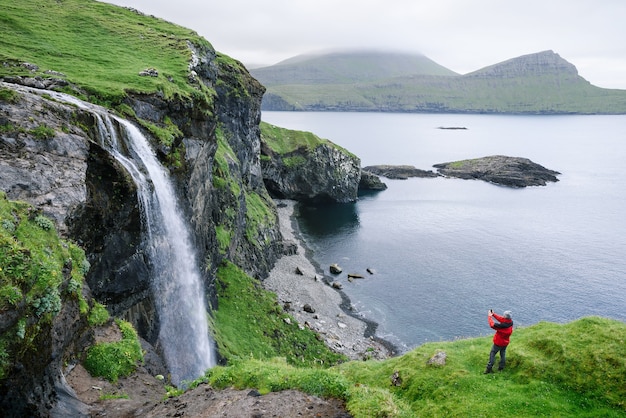 Ein Tourist fotografiert den Wasserfall Skardsafossur auf der Insel Vagar, Färöer-Inseln