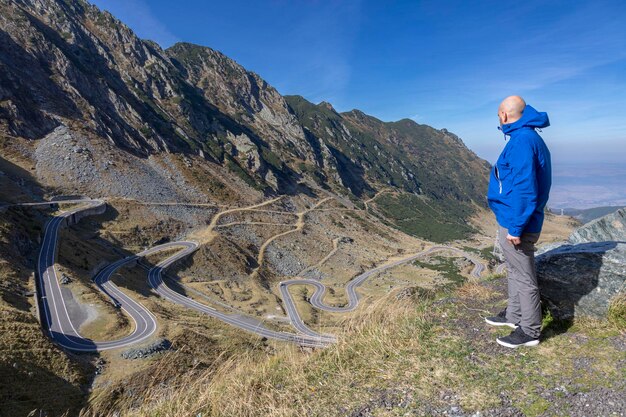 Foto ein tourist in einer blauen jacke blickt auf die straße in den bergen. rückansicht: carpathians ridge fagarash transfagarash road