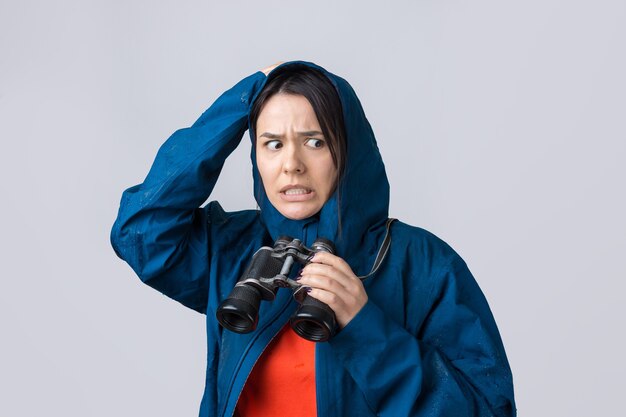 Ein Touristenmädchen in einem blauen Regenmantel hält ein Fernglas in den Händen und schaut in die Ferne, Spione.