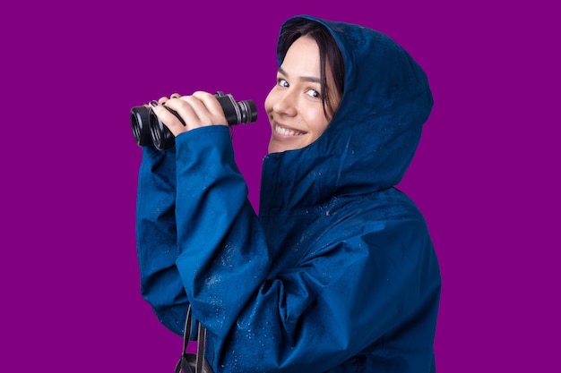 Ein Touristenmädchen in einem blauen Regenmantel hält ein Fernglas in den Händen und schaut in die Ferne