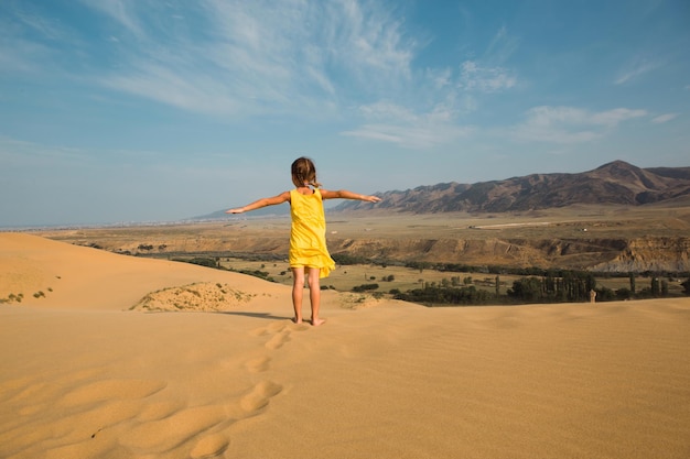 Ein Touristenmädchen in einem gelben Kleid läuft entlang einer Sanddüne in der Wüste Reisesehenswürdigkeiten der Düne von Dagestan Sarykum