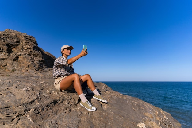 ein Touristenmädchen mit einem Rucksack im Sommer auf dem Gipfel eines Berges macht ein Selfie gegen den Hintergrund