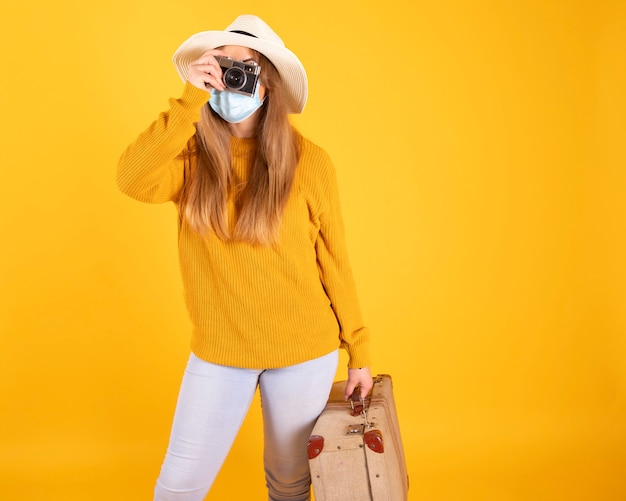 Ein Touristenmädchen mit einer medizinischen Maske, einem Koffer und einem Kamerahut kann nicht mit covid-19 reisen