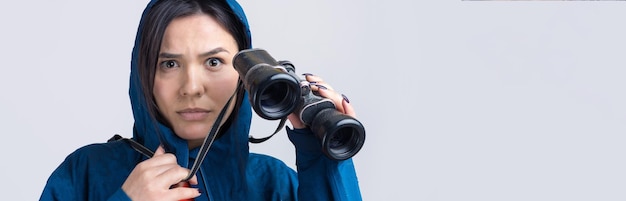 Ein touristisches Mädchen in einem blauen Regenmantel hält ein Fernglas in ihren Händen und schaut in die Fernspione