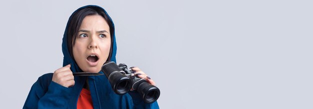 Ein touristisches Mädchen in einem blauen Regenmantel hält ein Fernglas in ihren Händen und schaut in die Fernspione