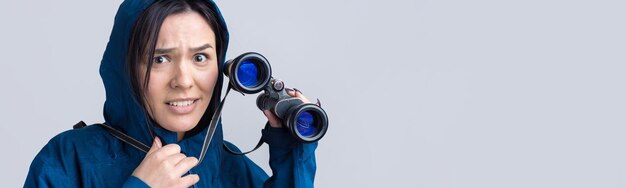 Ein touristisches Mädchen in einem blauen Regenmantel hält ein Fernglas in ihren Händen und schaut in die Fernspione