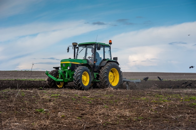 Ein Traktor der 90er Jahre John Deere 2850 mit einem hausgemachten Pflug bereitet das Feld für die Aussaat vor