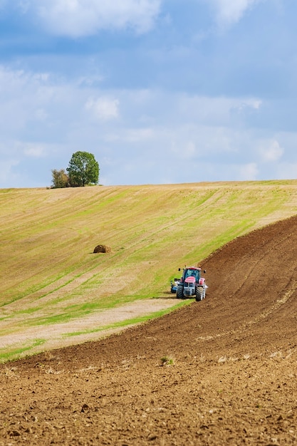 Ein Traktor mit einem großen Pflug pflügt ein Feld. Traktor mit landwirtschaftlichem Aufsatz. Vorbereitung des Landes für die Aussaat.