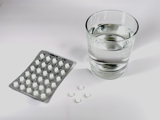 Ein transparentes Glas mit Wasser, eine Blase mit weißen Tabletten und mehrere Tabletten