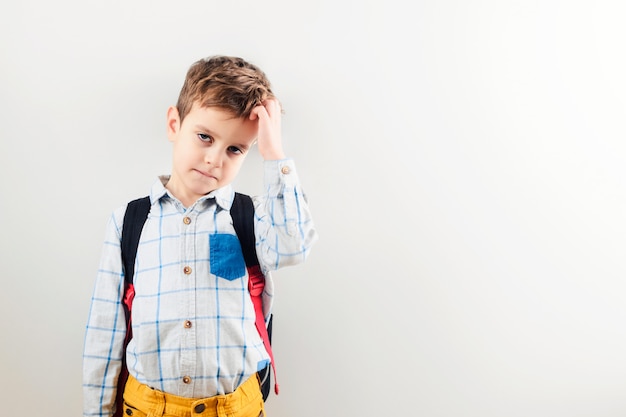 Ein trauriger Junge mit einem Rucksack gegen einen weißen Hintergrund.