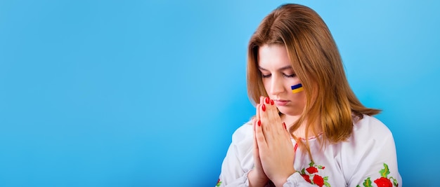 Ein trauriges junges ukrainisches Mädchen mit der Flagge der Ukraine auf ihrem Gesicht betet Die Konzeptteilnahme