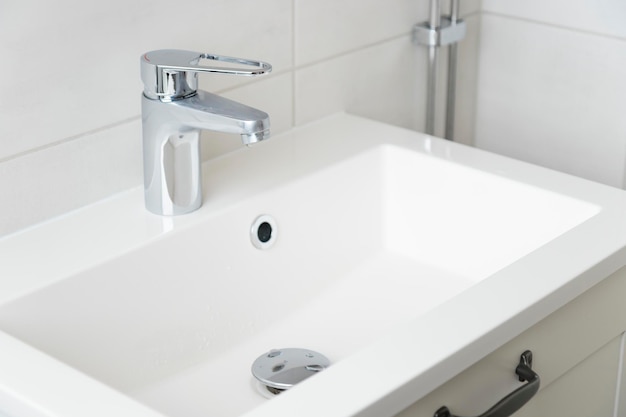 Ein Tropfen reines Wassers tropft aus dem Wasserhahn im weißen modernen Badezimmer.