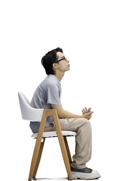 Ein Typ in einem grauen T-Shirt auf weißem Hintergrund sitzt auf einem Stuhl