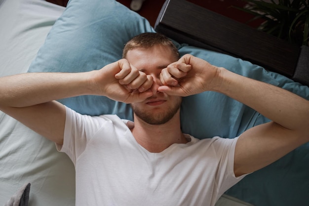 Foto ein typ liegt im bett und reibt sich die augen