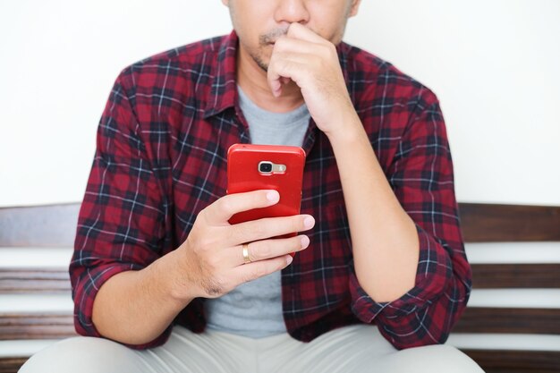 Ein Typ sitzt auf einer Bank und schaut mit ernster Geste auf sein Handy