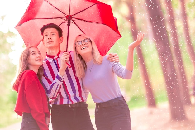 Ein Typ und zwei Mädchen unter einem roten Regenschirm im Wald bei Regen
