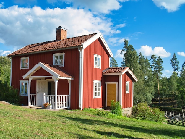 Ein typisches rot-weißes schwedisches Haus auf einer kleinen grünen Wiese und blauem Himmel mit kleinen Wolken. Landschaftsfoto aus Skandinavien