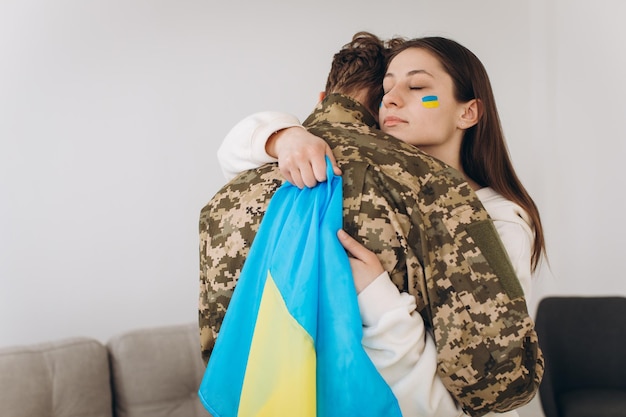 Ein ukrainisches Mädchen umarmt und hält eine gelb-blaue Flagge eines Militärs in Uniform und verabschiedet sich von ihm