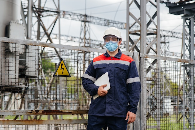 Ein Umspannwerkingenieur inspiziert moderne Hochspannungsgeräte in einer Maske zum Zeitpunkt der Pondämie. Energie. Industrie.