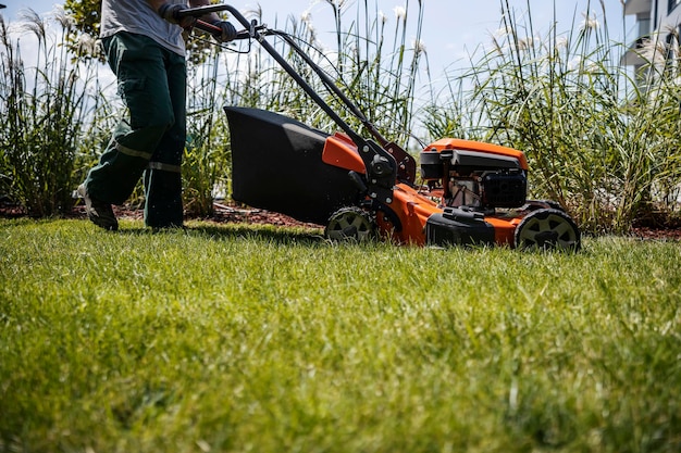 Ein unbekannter Mann mäht mit einer Grasschneidemaschine in einem öffentlichen Park einen Rasen