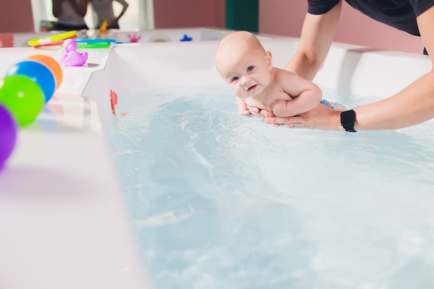 Ein Vater hilft als Kleinkind beim Schwimmunterricht im Pool.