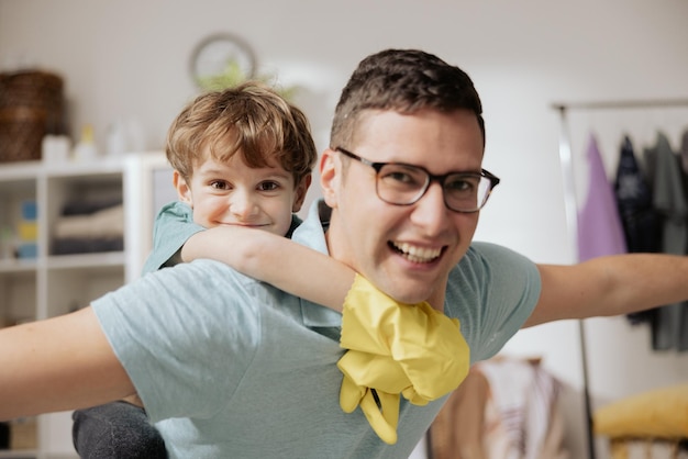 Ein Vater trägt seinen Sohn auf dem Rücken, während er Hausarbeiten vor Kindergummihandschuhen durchführt