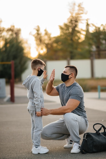 Ein Vater und ein Kind stehen auf einem Sportplatz in Masken nach dem Training während des Sonnenuntergangs