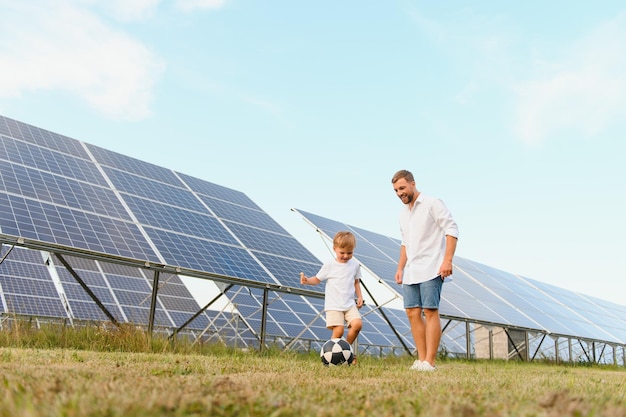 Ein Vater und sein kleiner Sohn spielen Fußball in der Nähe der Solaranlagen Das Konzept der erneuerbaren Energie