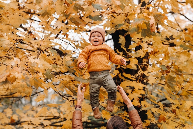 Foto ein vater wirft ein kind vor dem hintergrund des herbstlaubs in den park. vater wirft seinen sohn im herbstlaub hoch.