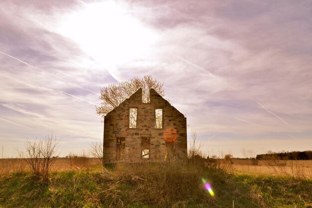 Foto ein verlassenes haus auf einem grasbewachsenen feld gegen einen bewölkten himmel